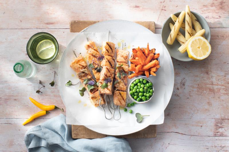 Salmon skewer marinated with spices and honey served with sweet potato chips, grilled corn on the cob and garden peas